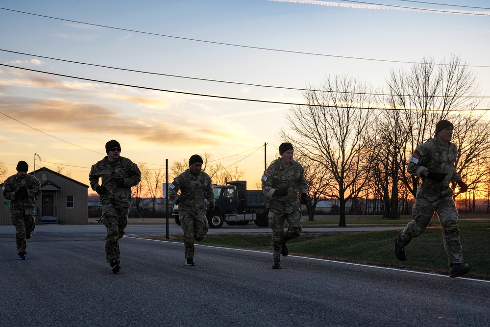 Cadets in camouflage uniforms running in formation at sunrise during physical training