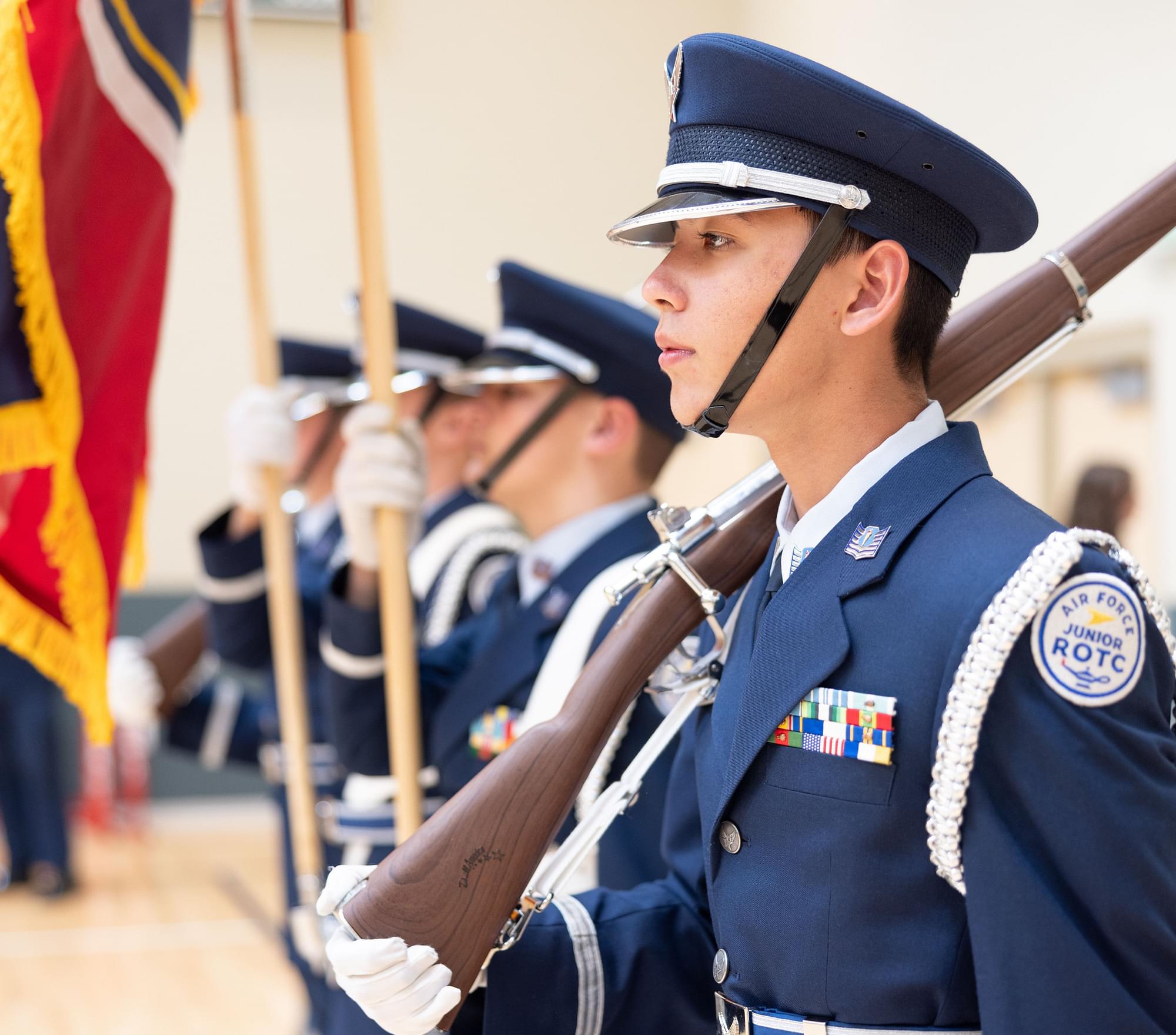 AFJROTC color guard cadets in navy dress uniforms with rifles, caps, and ceremonial flags