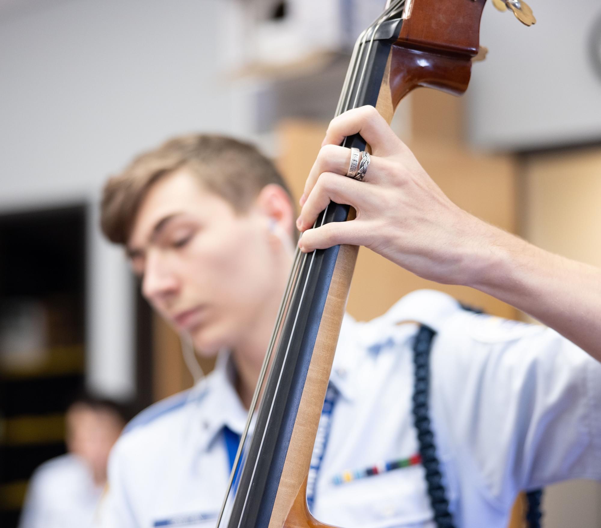 Male cadet in light blue AFJROTC uniform playing upright bass in music class