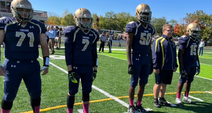 Trojans football players in navy and gold uniforms with gold helmets on game day