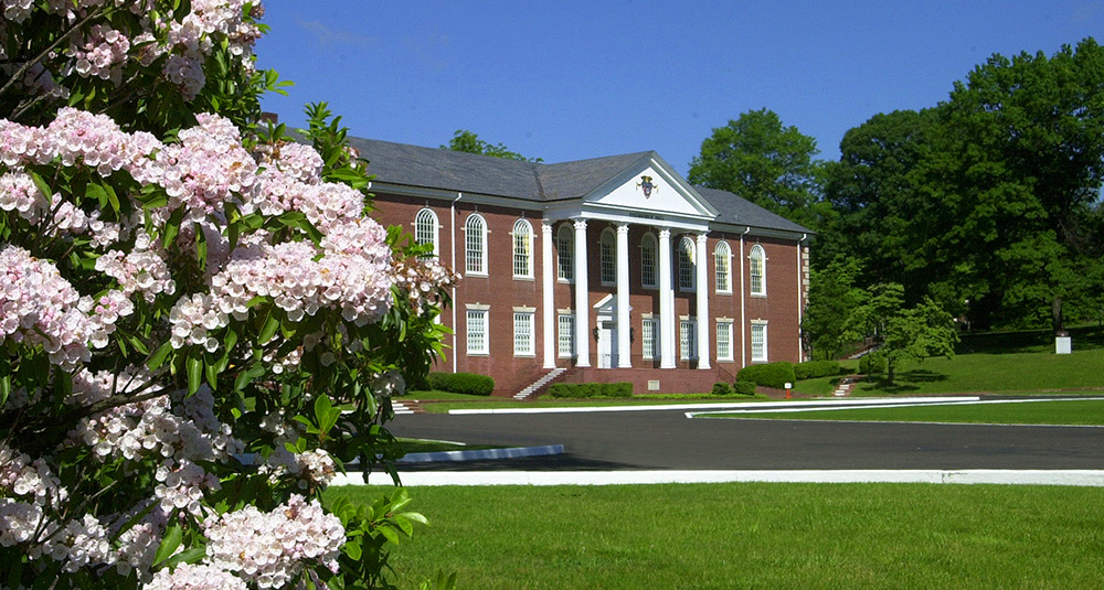 Stately brick academic building with white columns and pink flowering trees in spring