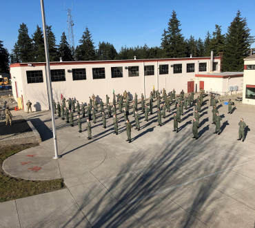 Aerial view of cadets in formation on parade ground with single-story campus buildings and evergreen trees