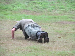 Cadet in camouflage uniform performing push-ups on grass field during physical training